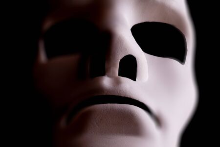 Blank mask close up in the shape of a human face, with black background.の写真素材