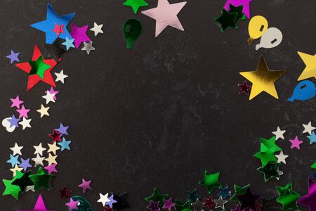 Party confetti stars and shaped of all colours scattered on a black table with copy spaceの写真素材