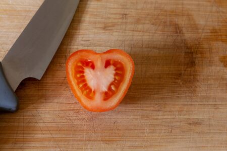 Tomato cut half, shaped like a heart, on a kitchen chopping board with big knife. Love fresh vegetables conceptの写真素材