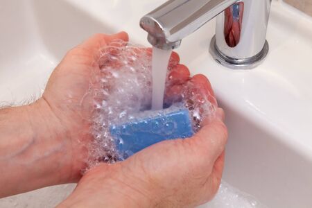 Washing hands with bar of soap under a running water from a chrome tap and sink. Stop spreading viruses, germs and bugs conceptの写真素材