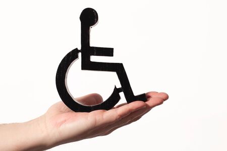 Disabled black shape cutout from wood sat on an open hand. Disability helping hand concept on a...