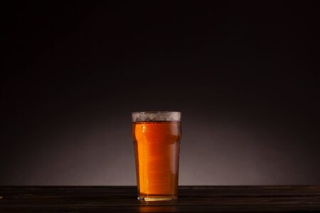 Pint of beer still life setup with dark table and minimal lighting. Dark background with copy space and text space.の写真素材