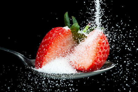 Fresh strawberry sliced on a spoon with sugar granules pouring over it. Diet and hidden sugar conceptの写真素材