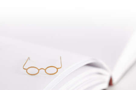 Tiny reading glasses on an open book with blank pages. White background with text space. No wordsの写真素材