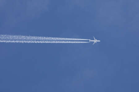 One passenger plane high in the sky with chemtrails with a blue skyの写真素材