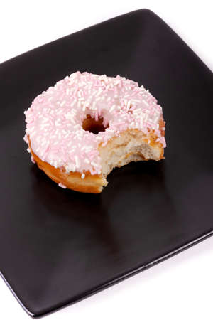 Frosted donut with a bite taken out of it, on a black square plate, with a white background.の写真素材