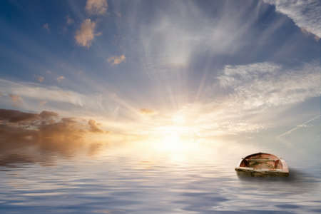 Lost at sea, old rowing boat bobbing around at sea in a tranquil sunset with calm ocean water. No land only seascape and beautiful clouds.の写真素材