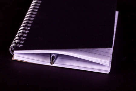 Notepad and pen close with spiral bound lined pages. Business memo and note taking concept on black backgroundの写真素材