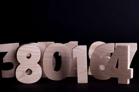 Large random wooden numbers standing up overlapping. Hardwood characters on a black background with copy spaceの写真素材