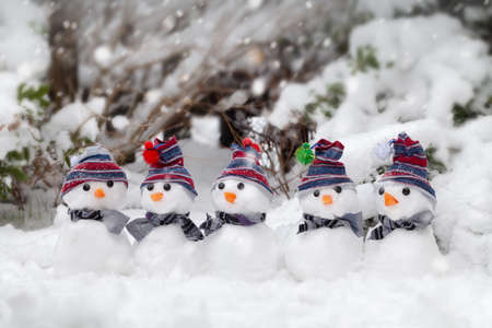 Five little cute snowmen dressed in hats and scarfs sat in the snow in winter. Cold and freezing snowing weather. Christmas holiday backgroundの写真素材