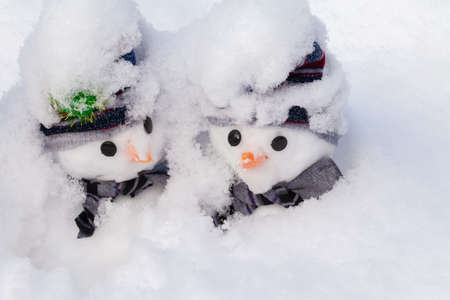 Two little snowmen buried deep in a winters snow fall. Cute characters for Christmas fun and humour wearing hats and scarfsの写真素材