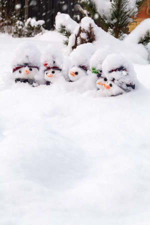 Fun little snowmen covered in a fresh snowfall wearing hats and scarfs and carrots noses. Winter snow fun and homour landscape with white spaceの写真素材