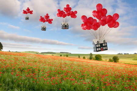 Houses tied to red balloons floating over a beautiful poppy field. Moving house and estate agent conceptの写真素材