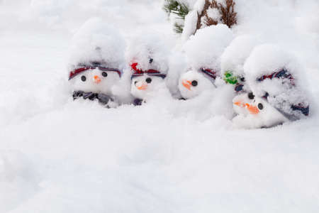 Five little cute snowmen covered in a fresh snowfall wearing hats and scarfs and carrots noses. Winter snow fun and homour landscapeの写真素材