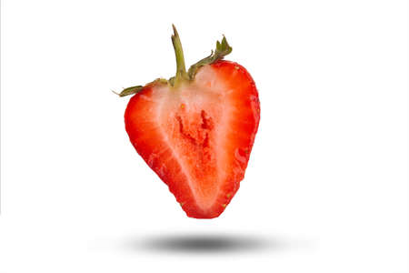 Fresh red half strawberry isolated on a white background floating with a shadow. Delicious fruit cut open close up with pips and stalkの写真素材