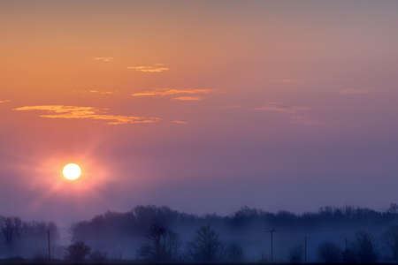 Beautiful sunrise over rural landscape with cold misty trees and orange skiesの写真素材
