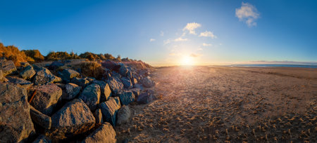 Stunning sunset at Brancaster beach with sand and sea defence rocks. Panoramic scenic landscape in North Norfolkの写真素材