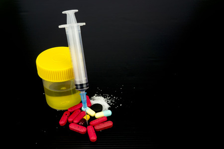 Urine sample bottle, syringe and pills isolated on a black background with shallow depth of field (dof)の写真素材