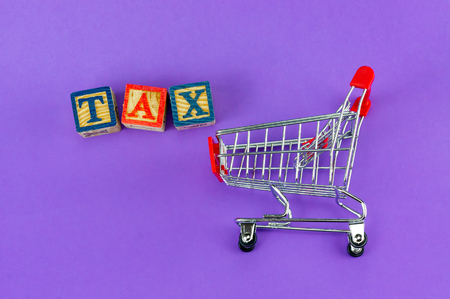 TAX and Taxation on household goods concept. Trolley with alphabet (T.A.X) block on purple background.の写真素材