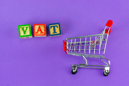 VAT (Value-Added Tax) on household goods concept. Trolley with alphabet (V.A.T) block on purple background.の写真素材