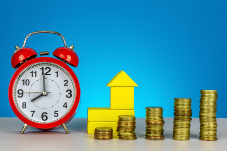 Saving for future. Saving for dream house and time to saving concept. Clock and stacking coin on blue background.の写真素材
