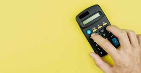 Close up hand using calculator on yellow background. Copy space.の写真素材