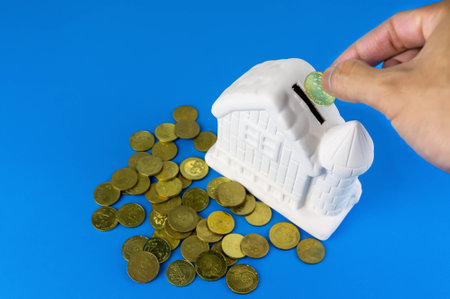 Closeup of hand putting coin in ceramic house piggy bank. Savings, investment and development concept or other your content.の写真素材