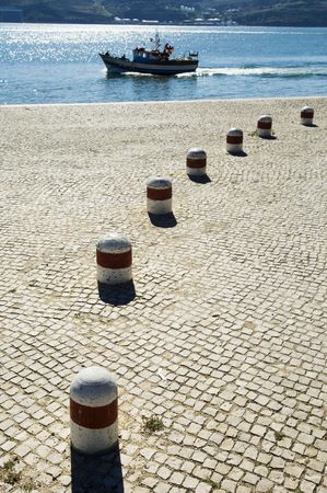 A view of a small fishing boat as it passes a large cobblestone quay on its way out of the harbor on the Tagus River in Lisbon, Portugal.の写真素材