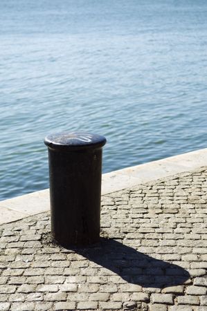 A view of a short, cylindrical metal post permanently attached to a pier or quay, often called a bollard to which a ship is tied while docked.の写真素材