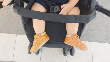 The baby wears brown shoes that are in the stroller