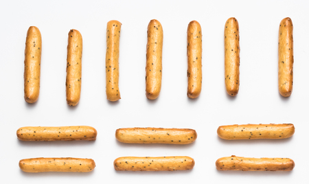 Crispy breadsticks with poppy seeds arranged in rows on a white backgroundの写真素材