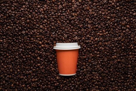 Orange disposable cup to go, on the background of coffee beans with empty space for textの写真素材