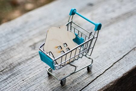 Toy wooden house with a shopping trolley on a natural wooden background. Concept photo about buying...