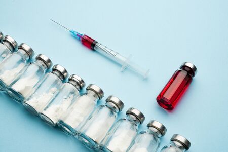 Row of medical vials and syringe. Glass bottles with powder for injection and one with red potion on a light background.の写真素材
