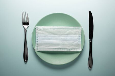 Disposable medical mask on a round plate with a knife and fork. Concept photo.の写真素材