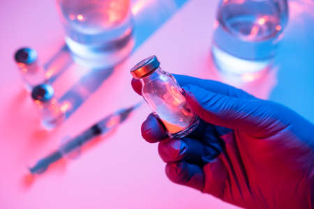 The doctor holds an ampoule with a vaccine. Hand in medical glove with the glass ampoule. Concept of...