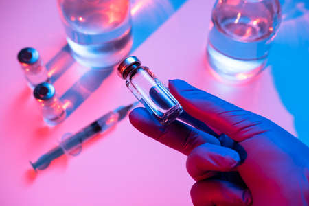The doctor holds an ampoule with a vaccine. Hand in medical glove with the glass ampoule. Concept of...
