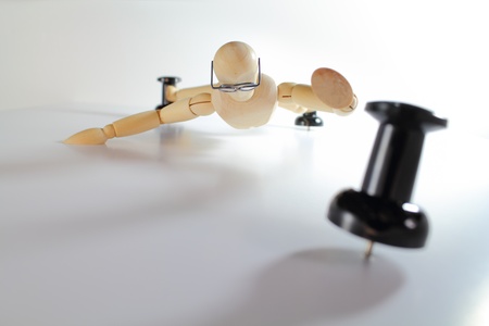 Wooden artist manikin with glasses scaling a white wall on black pushpins.
