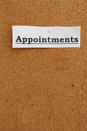 White strip of paper with the word appointments pinned to a cork board.の写真素材