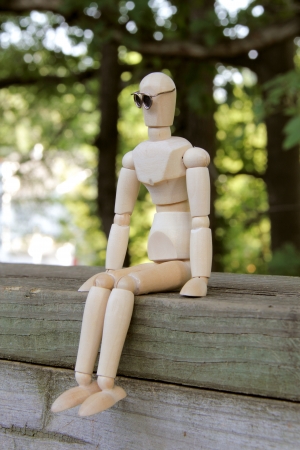 Wooden artist manikin sitting on a wooden fence and thinking reflectively の写真素材