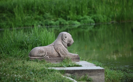 the old stone sculpture of a lion on a green backgroundの写真素材