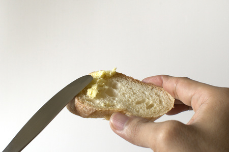 A man is spreading a butter on a sliced baguette using a knife against white backgroundの写真素材