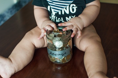A baby boy is holding a jar filled with coinsの写真素材