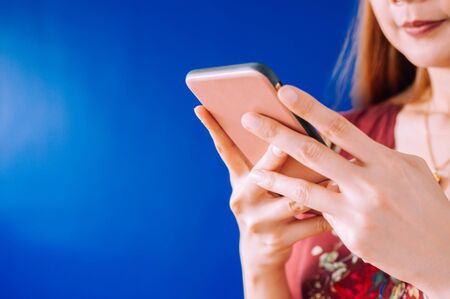 A young woman is using a mobile phone on a blue backgroundの写真素材