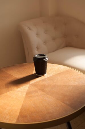 A disposable cup of coffee on a wooden table indoor with sunbeamの写真素材