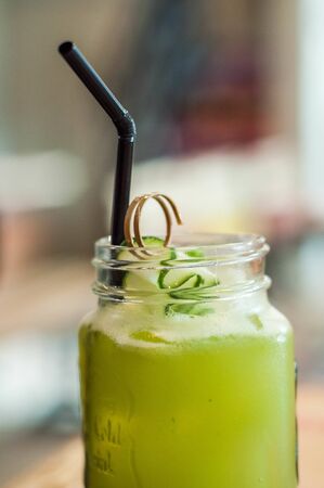 A close-up view of cucumber and lemon juice with plastic straw on a wooden tableの写真素材