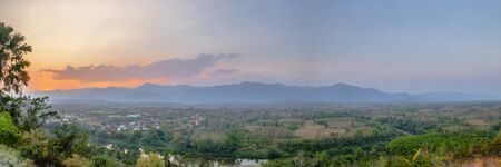 Panorama view of the village at sunset. The landscape view of a small village situated on a green hill in a valley surrounded by mountains and rivers.の写真素材