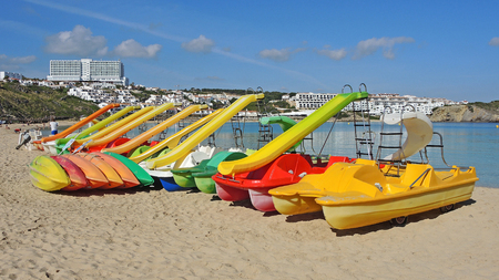 Group of colorful pedal boats with and without slide on the beach of Arenal d'en Castell, Menorca Island, Spain.の写真素材