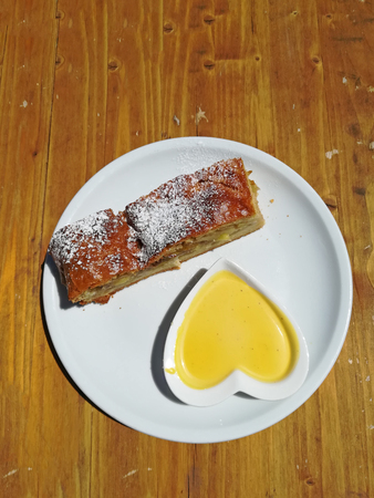 Homemade apple strudel with custard topping in heart shaped dishの写真素材