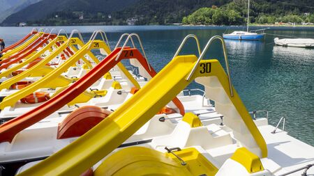Group of red and yellow pedal boats with slide at Ledro Lake in Italy. A natural alpine lake. Summer time. Touristic destinationの写真素材